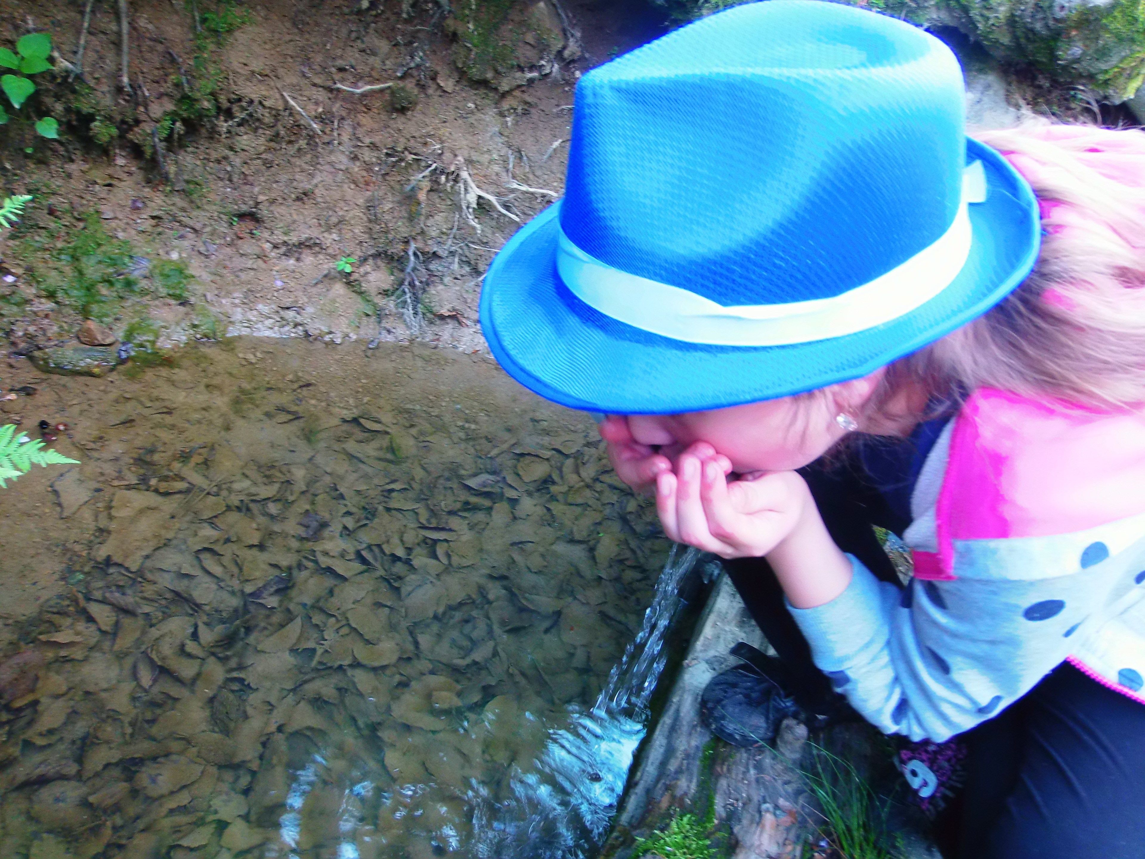 Una persona con sombrero azul y prenda con estampado de lunares cerca de un cuerpo de agua.
