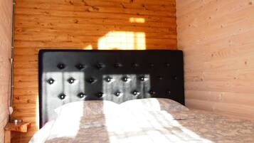 A room with a bed, wooden walls, and a window allowing sunlight to enter.