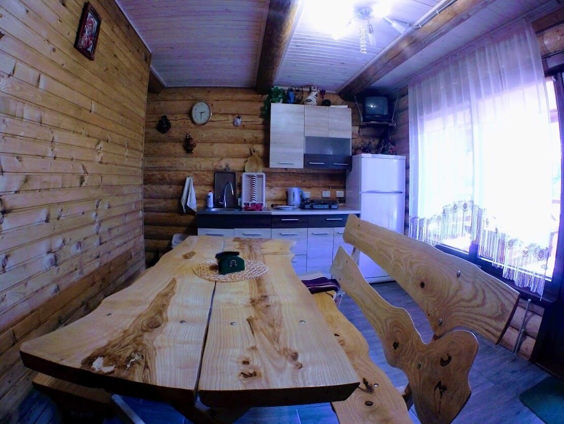 Un interior de madera con una mesa de comedor, bancos, una zona de cocina con armarios, un reloj y un televisor.