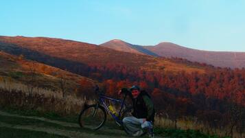 A person posing with a bicycle on a dirt path with a mountainous backdrop.
