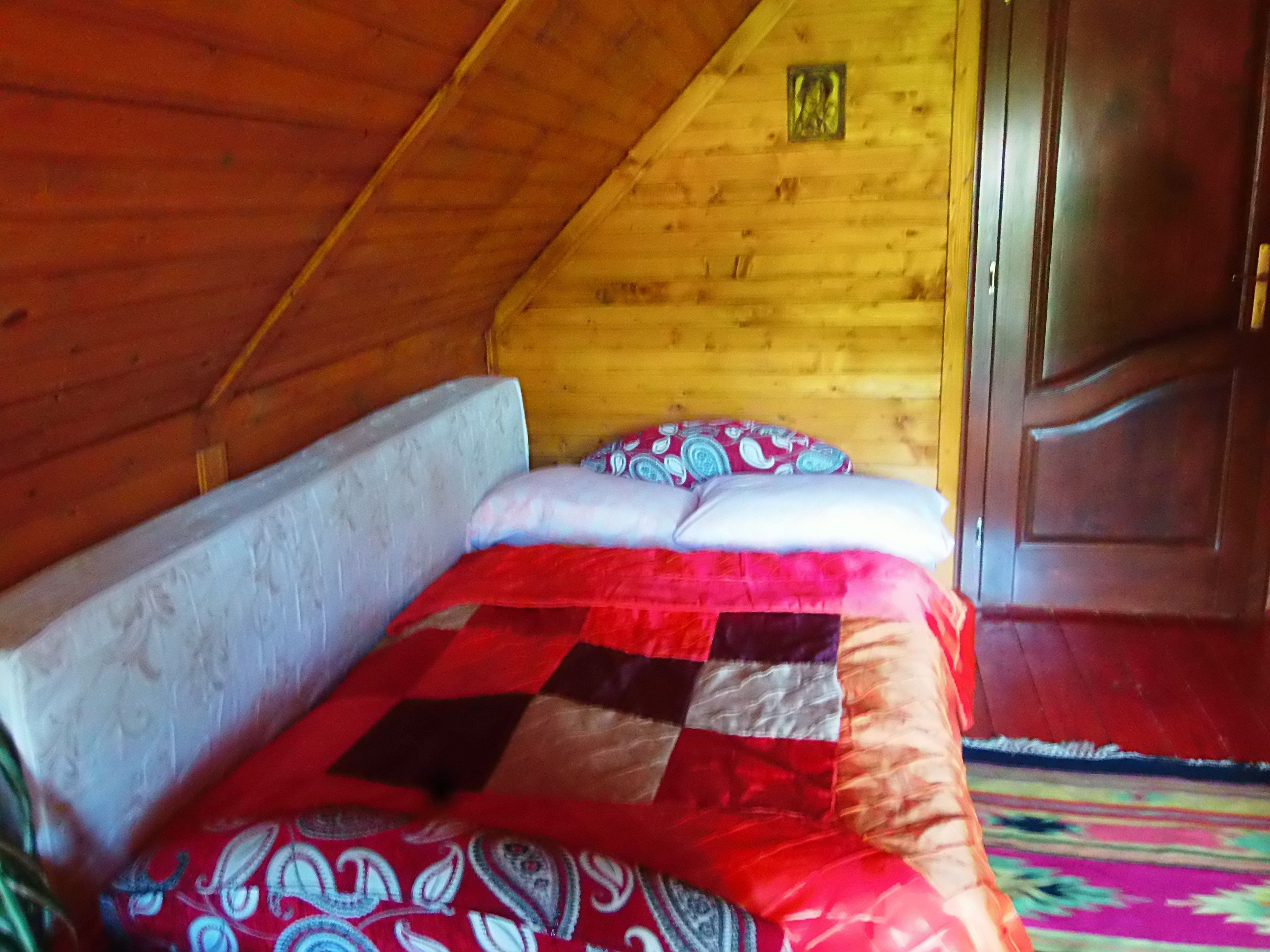 A bedroom with a wooden ceiling, a bed with patterned bedding, and a wooden door.