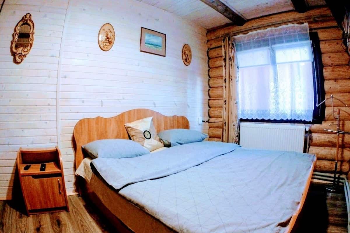 Een slaapkamer in een houten chalet met een bed, nachtkastje en een raam met gordijnen.