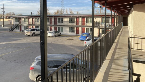 A motel with a covered parking area, multiple cars parked, and a clear view of the surrounding area.