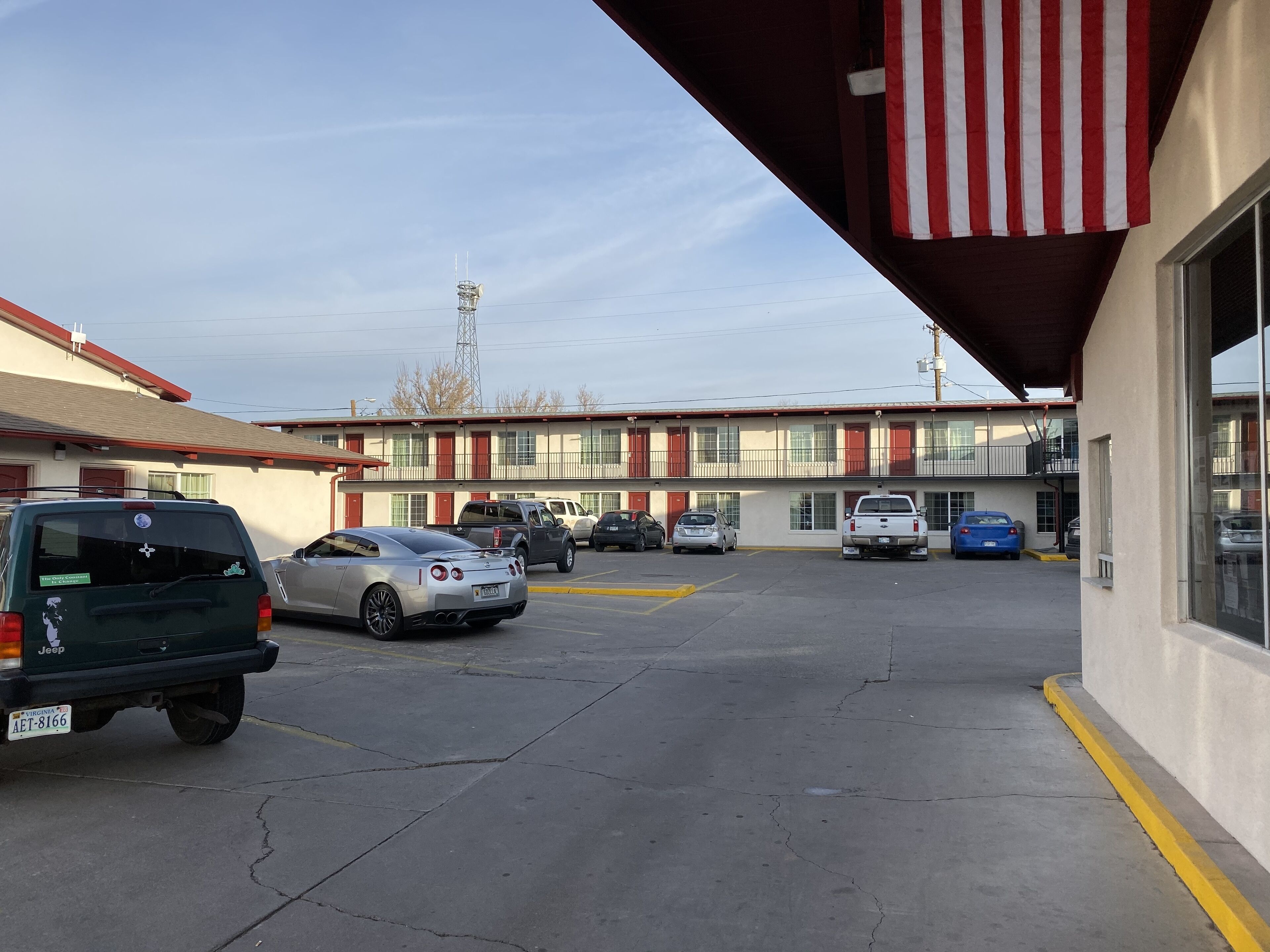 A motel with a parking lot, several parked cars, and a building with a red and white striped awning.