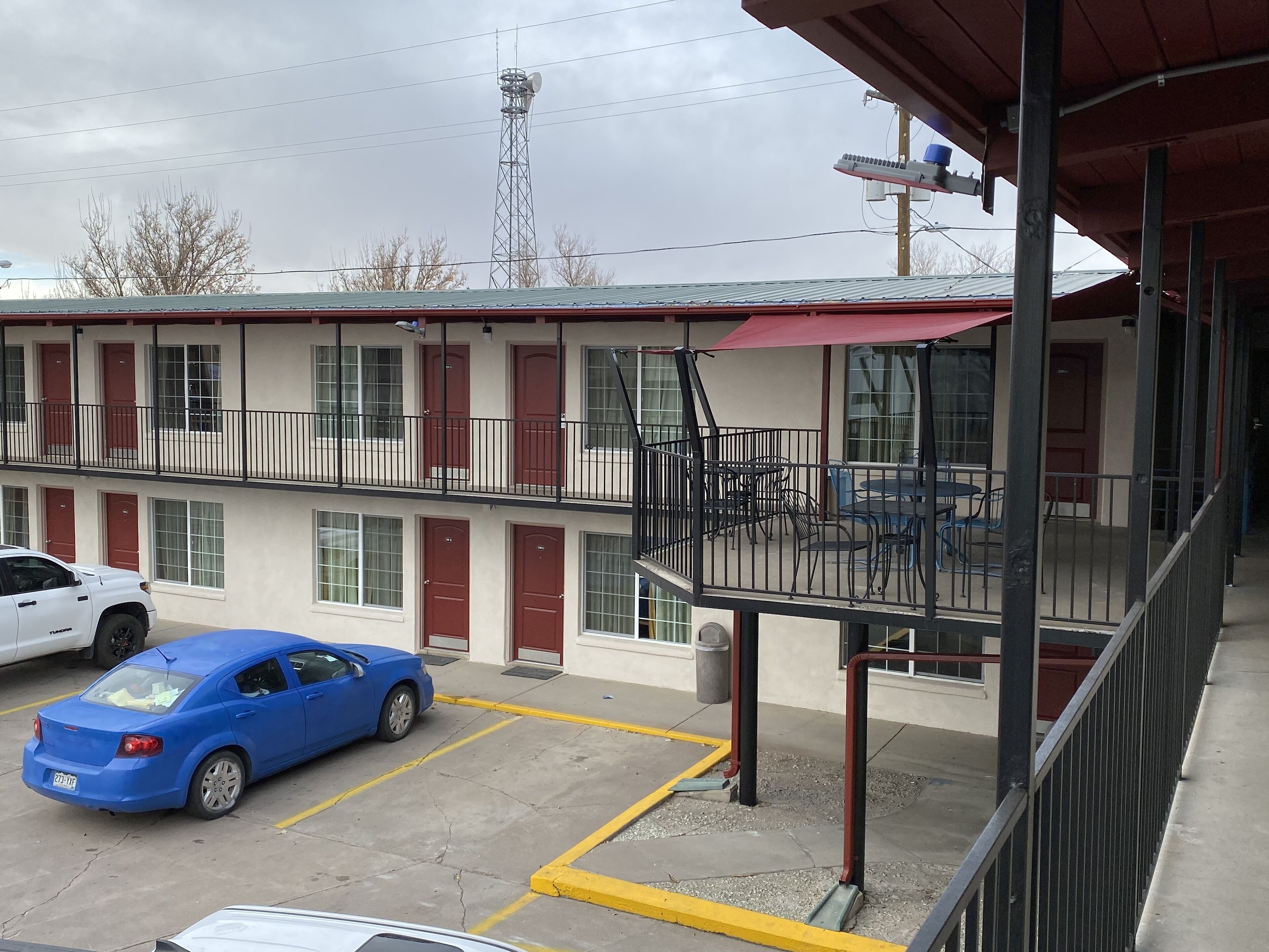 Un motel con una estructura de dos pisos, un área de estar al aire libre cubierta y un estacionamiento.