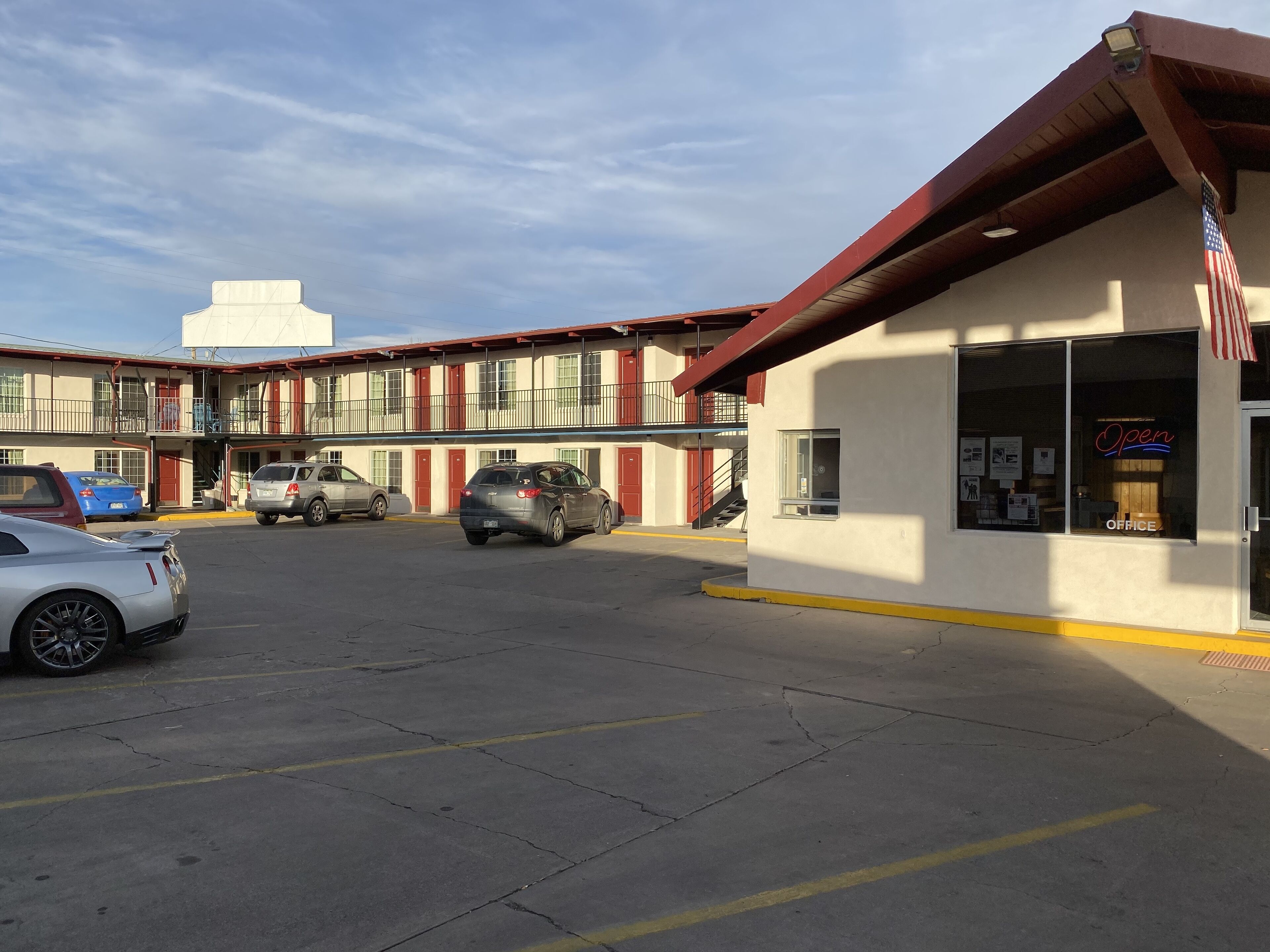 A parking lot with several cars, a building with a red roof, and an American flag.