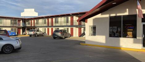 A parking lot with several cars, a building with a red roof, and an American flag.
