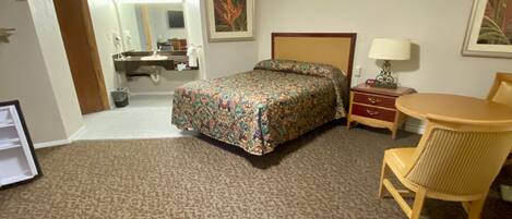Ein Hotelzimmer mit Bett, Schreibtisch, Stuhl, Lampe und einem durchgegangenen Tür sichtbaren Badezimmer.