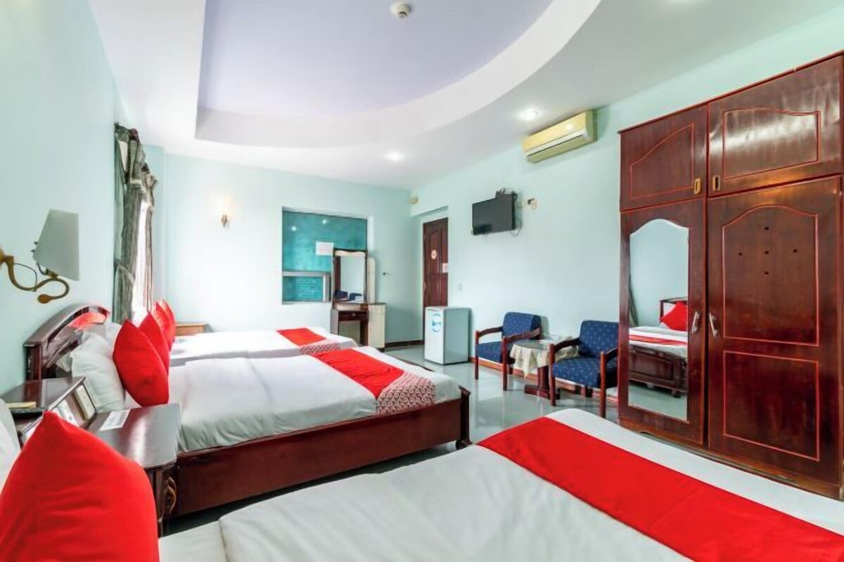 A hotel room with two beds, a desk, a chair, a wardrobe, and a television.