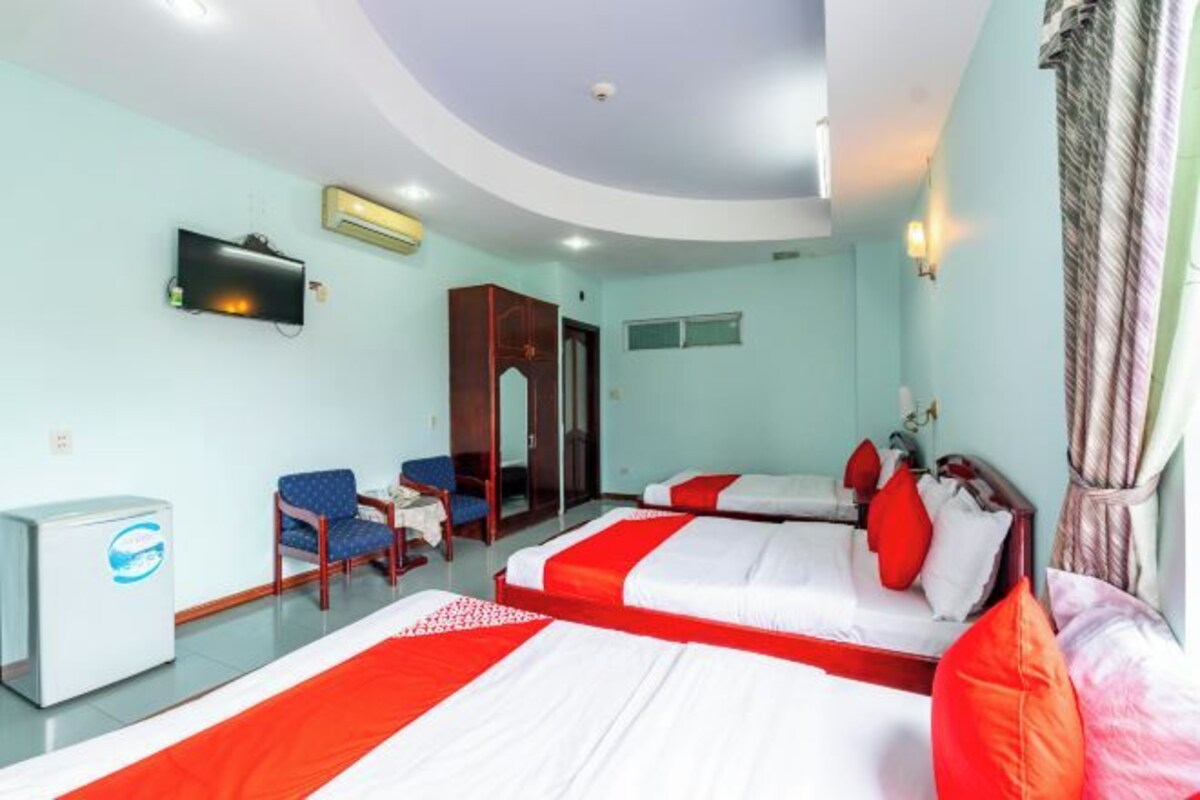 A hotel room with two beds, a television, a refrigerator, and a desk with a chair.