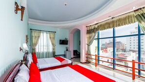 Habitación de hotel con dos camas, televisor, escritorio y balcón con vista a la ciudad.