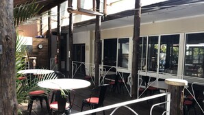 Un espace extérieur aménagé en terrasse, avec des tables et des chaises rondes, des poutres en bois et de grandes fenêtres.
