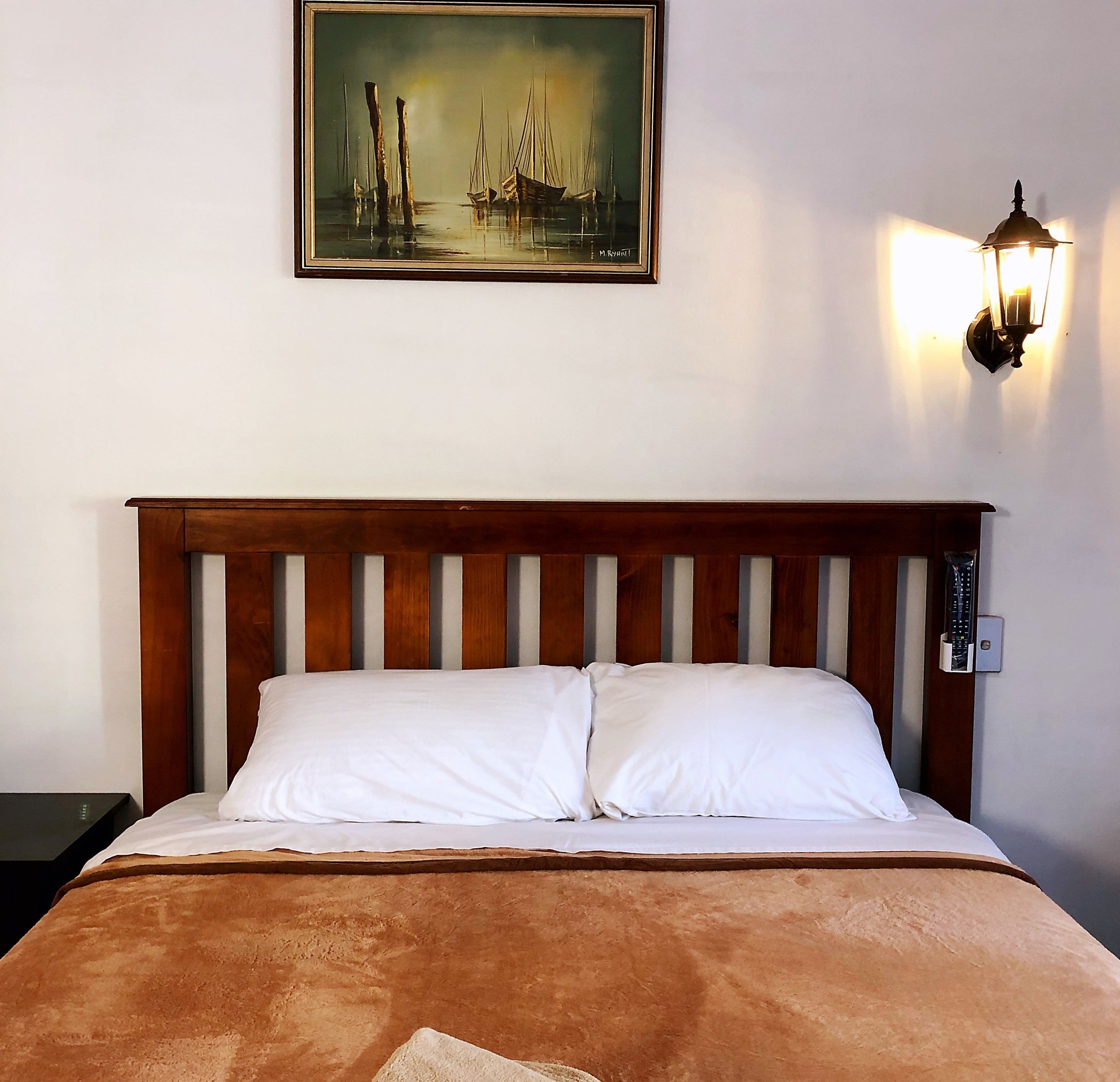 Una cama con cabecera de madera, almohadas blancas y una manta marrón.