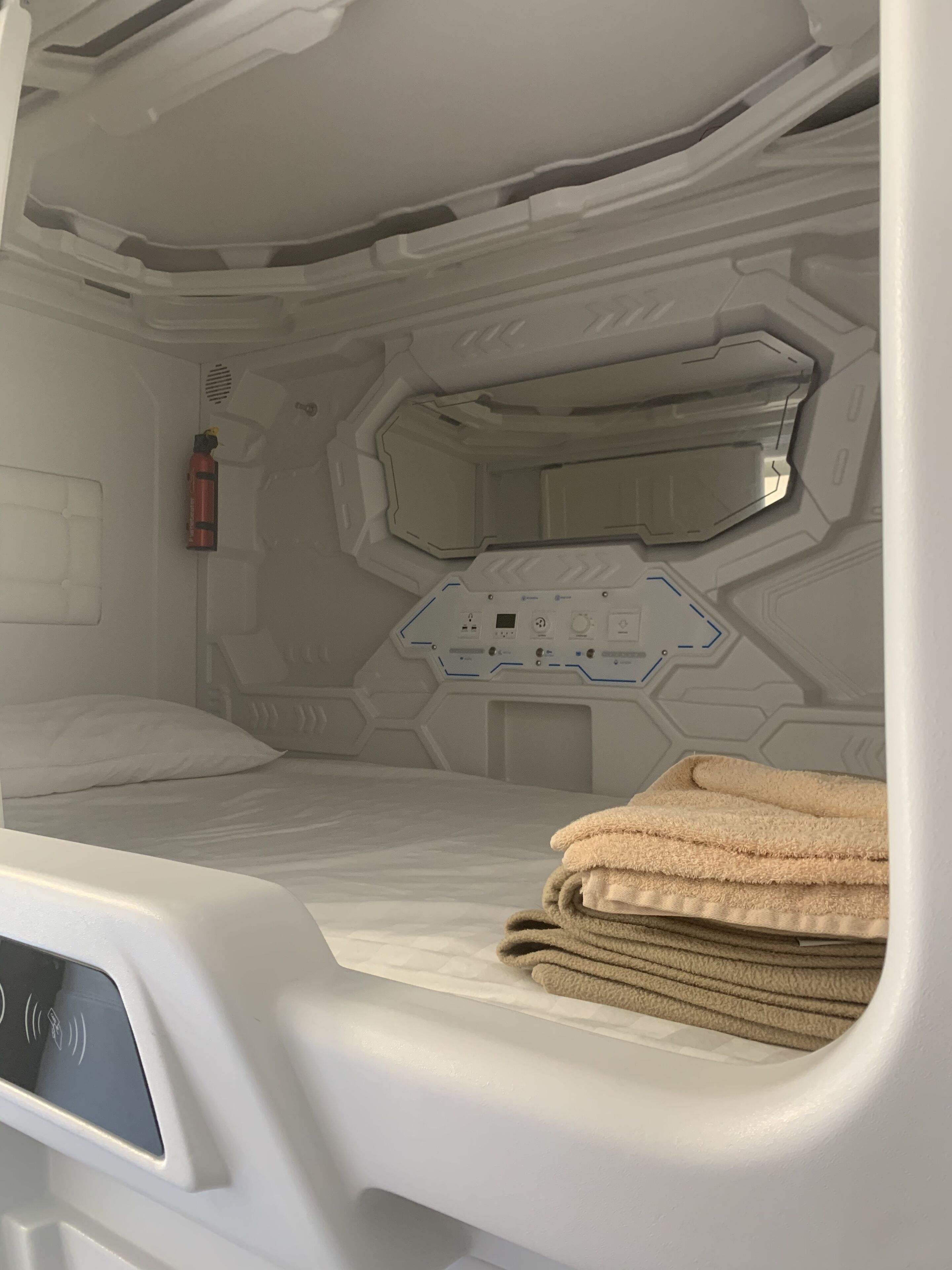 Una habitación futurista con una cama, un panel de control y un extintor.