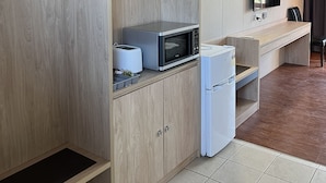Une chambre d’hôtel compacte comprenant un coin cuisine, un lit avec une tête de lit, un téléviseur à écran plat et une salle de bain avec un rideau de douche.