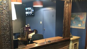 Une salle de bain avec un grand miroir, un lavabo et un meuble-lavabo en bois. On aperçoit une porte au fond et une carte accrochée au mur.