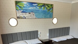 Une chambre d’hôtel avec deux lits, un tableau représentant une scène de plage et un miroir rond.