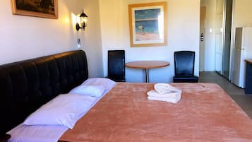 A hotel room with a bed, two chairs, a small table, a painting on the wall, and a refrigerator.