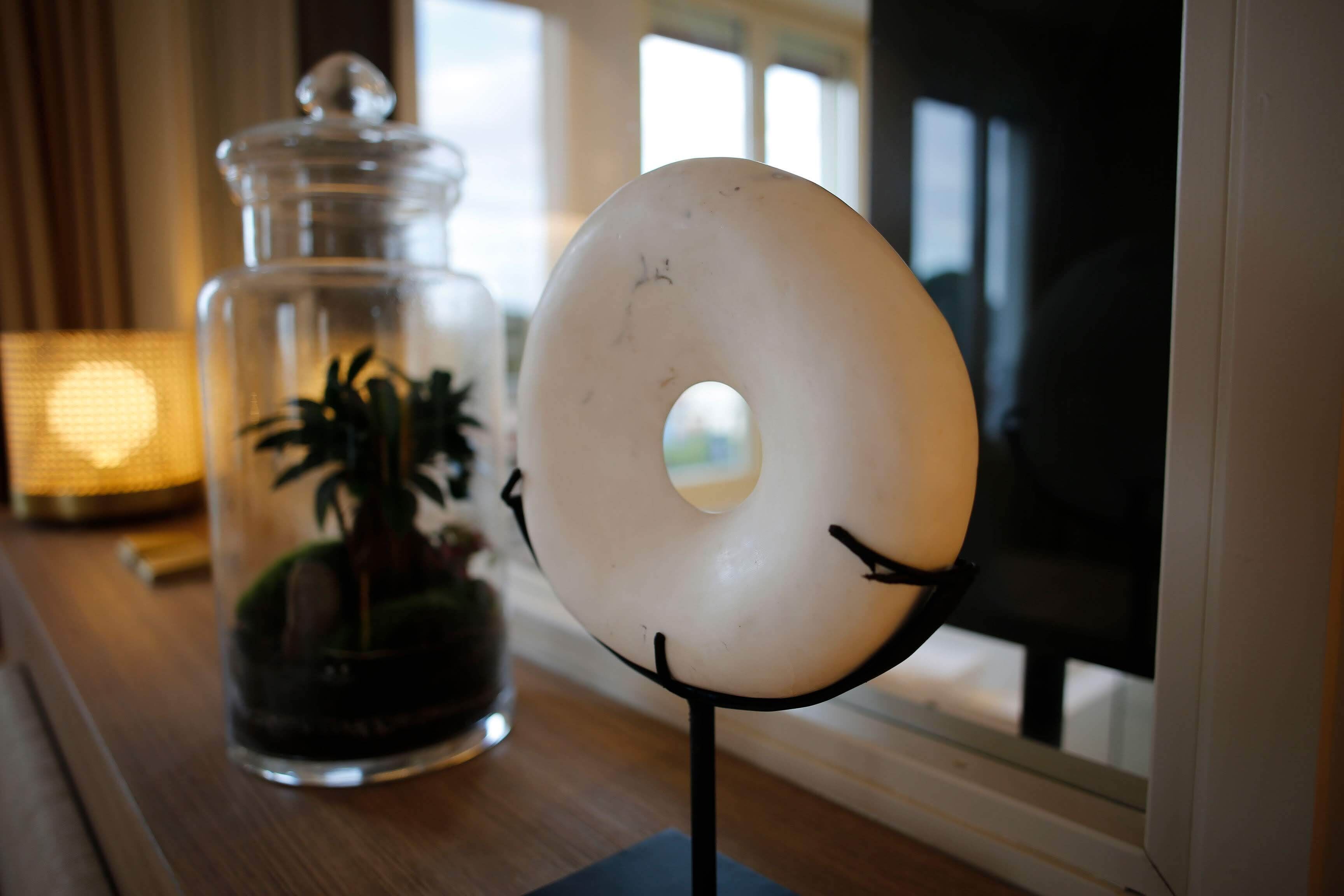 A donut-shaped object on a stand next to a glass jar with a plant inside.