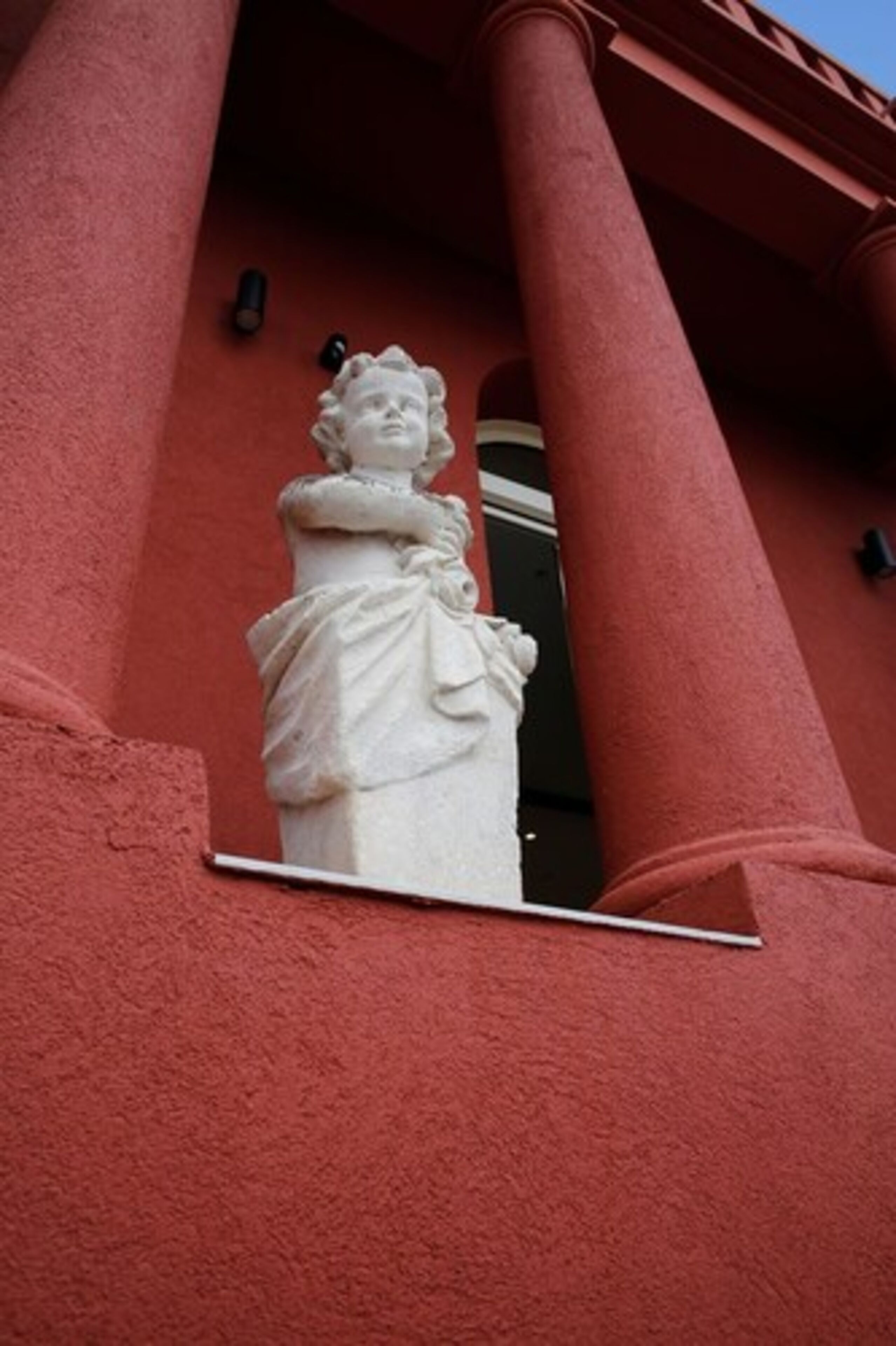 A white statue of a woman in a dress mounted on a building with red columns.