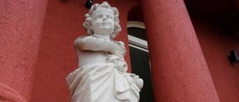 A white statue of a woman in a dress mounted on a building with red columns.