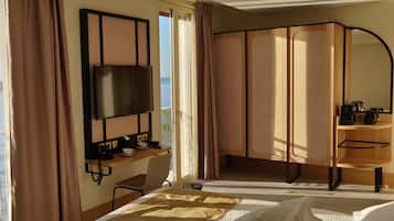 A modern hotel room with a large TV, a balcony with a view of the water, and a wooden cabinet with a kettle.