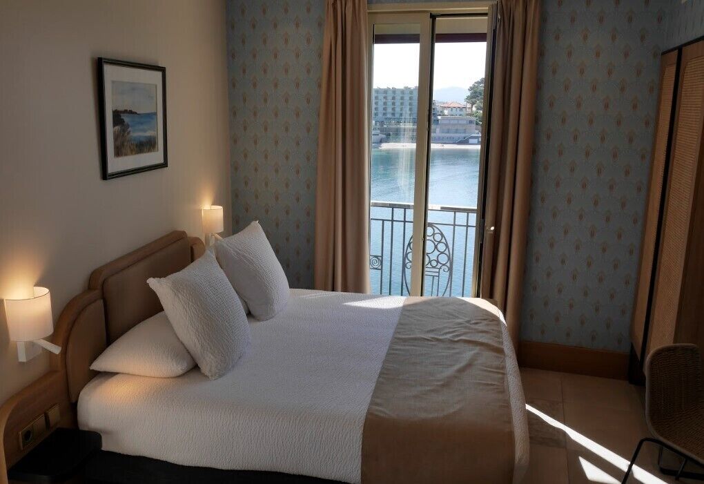 A hotel room with a large bed, a view of a body of water, and a balcony.