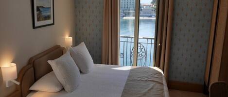 A hotel room with a large bed, a view of a body of water, and a balcony.