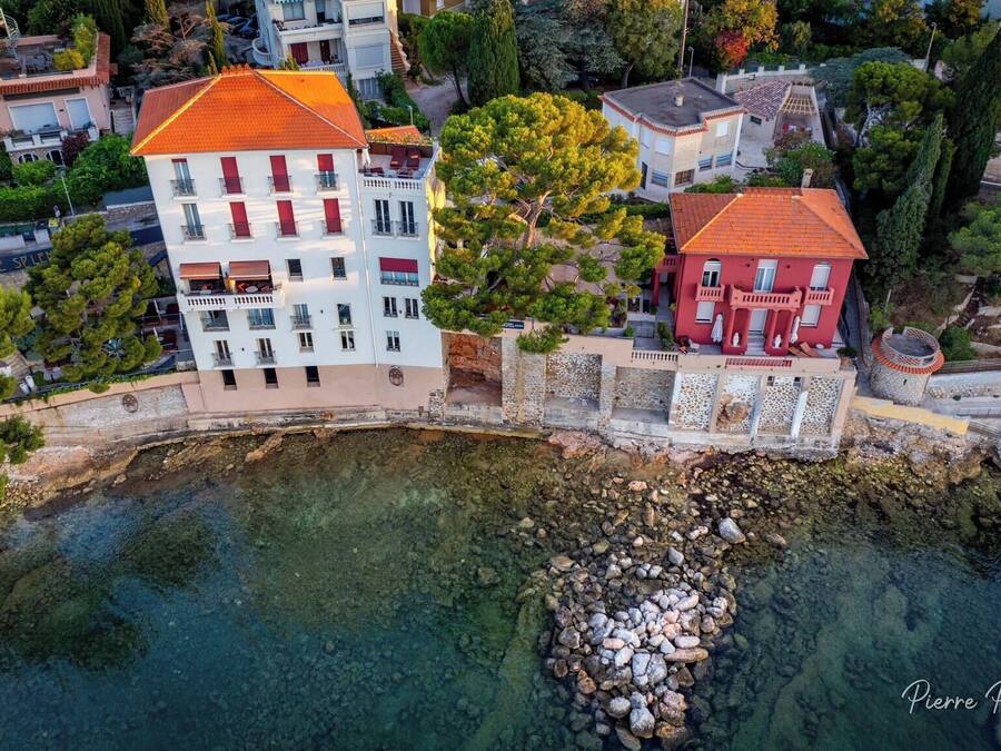 Vista aerea di un hotel costiero con diversi edifici, acque limpide e un litorale roccioso.