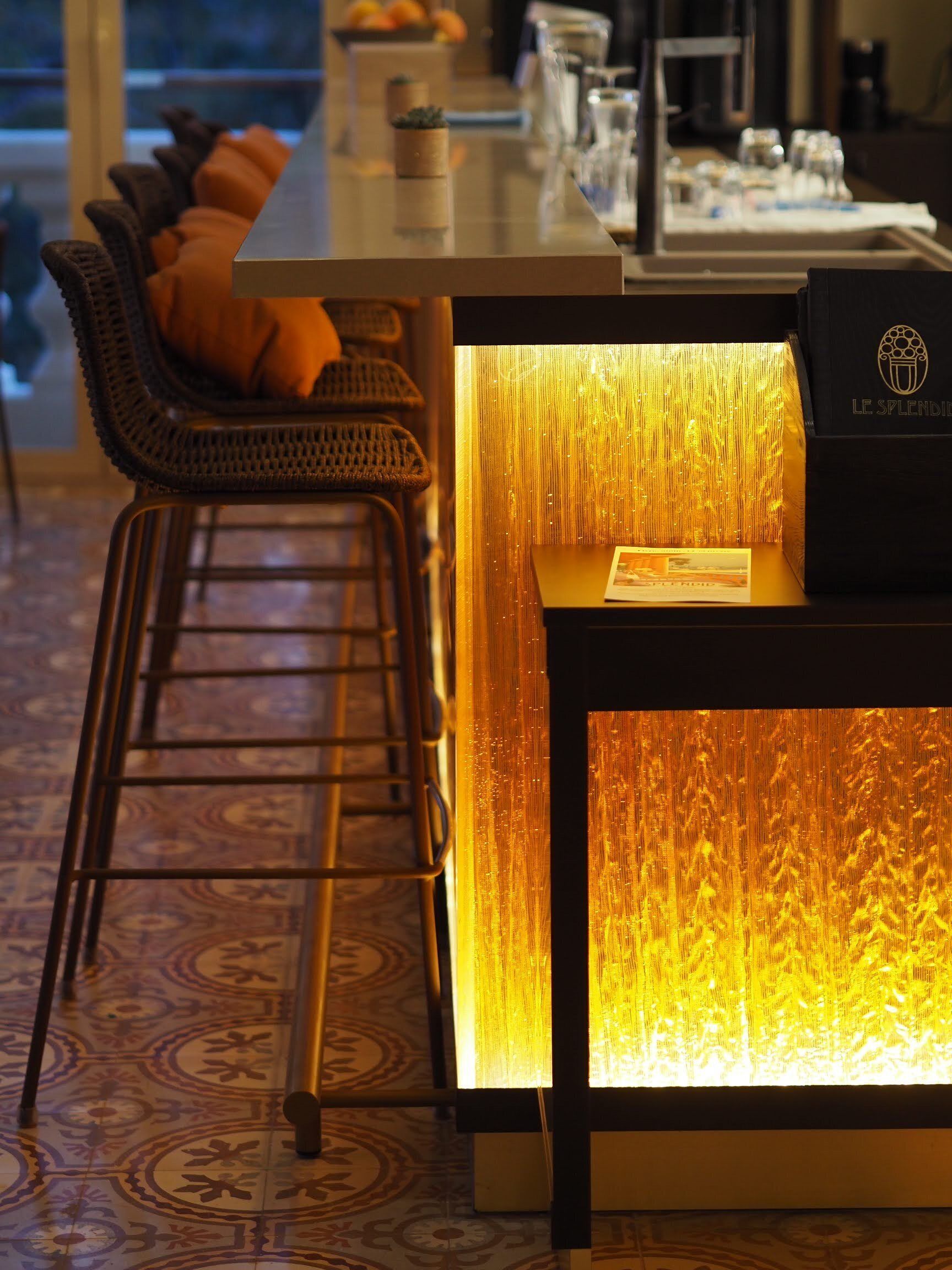 Un espace bar au design moderne, comprenant un comptoir, des sièges avec des fauteuils rembourrés et un panneau lumineux décoratif.