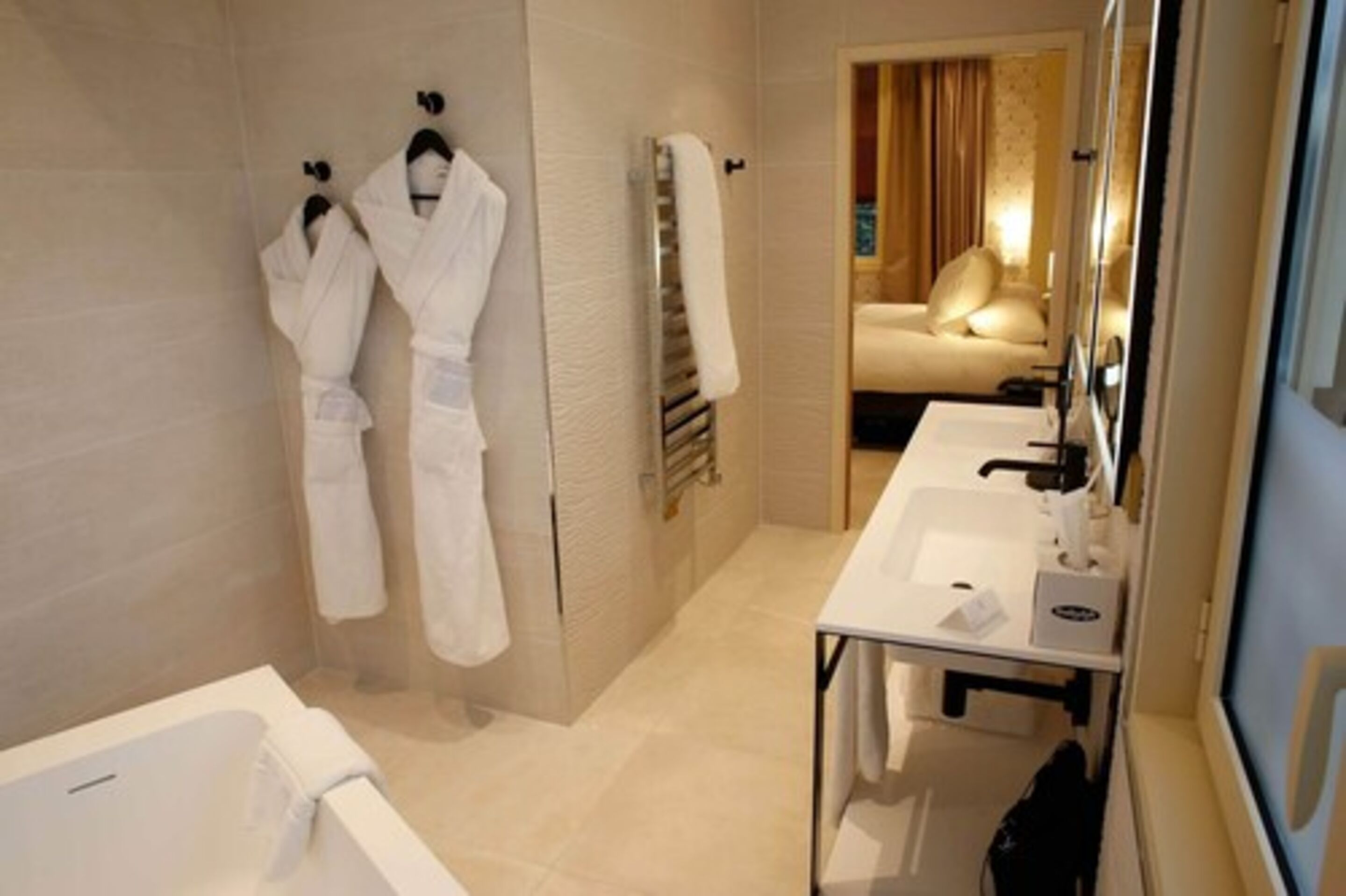A modern bathroom with a bathtub, a double sink, and two white robes hanging on the wall.