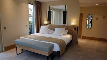 A modern hotel bedroom with a large bed, bedside lamps, a bench, and a large mirror.