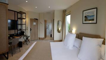 Habitación de hotel con cama, escritorio con computadora, televisor y baño visible a través de una puerta abierta.