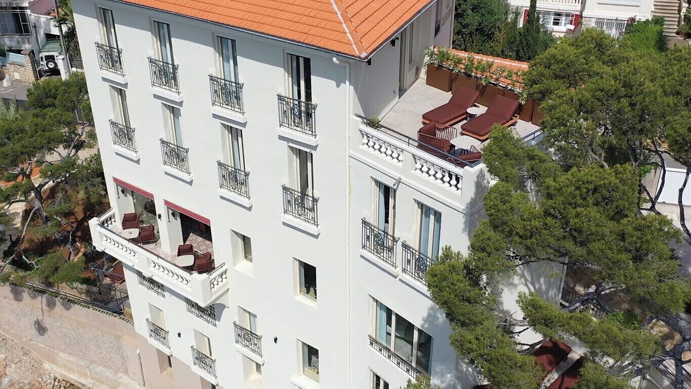 Un immeuble à plusieurs étages doté de balcons, d’une terrasse sur le toit et entouré d’arbres.