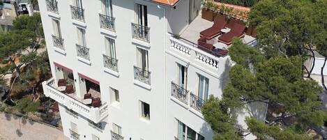 A multi-story building with balconies, a rooftop terrace, and surrounding trees.