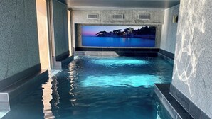 Une piscine à l’eau claire, une vue sur un coucher de soleil sur l’eau et un mur de pierre.