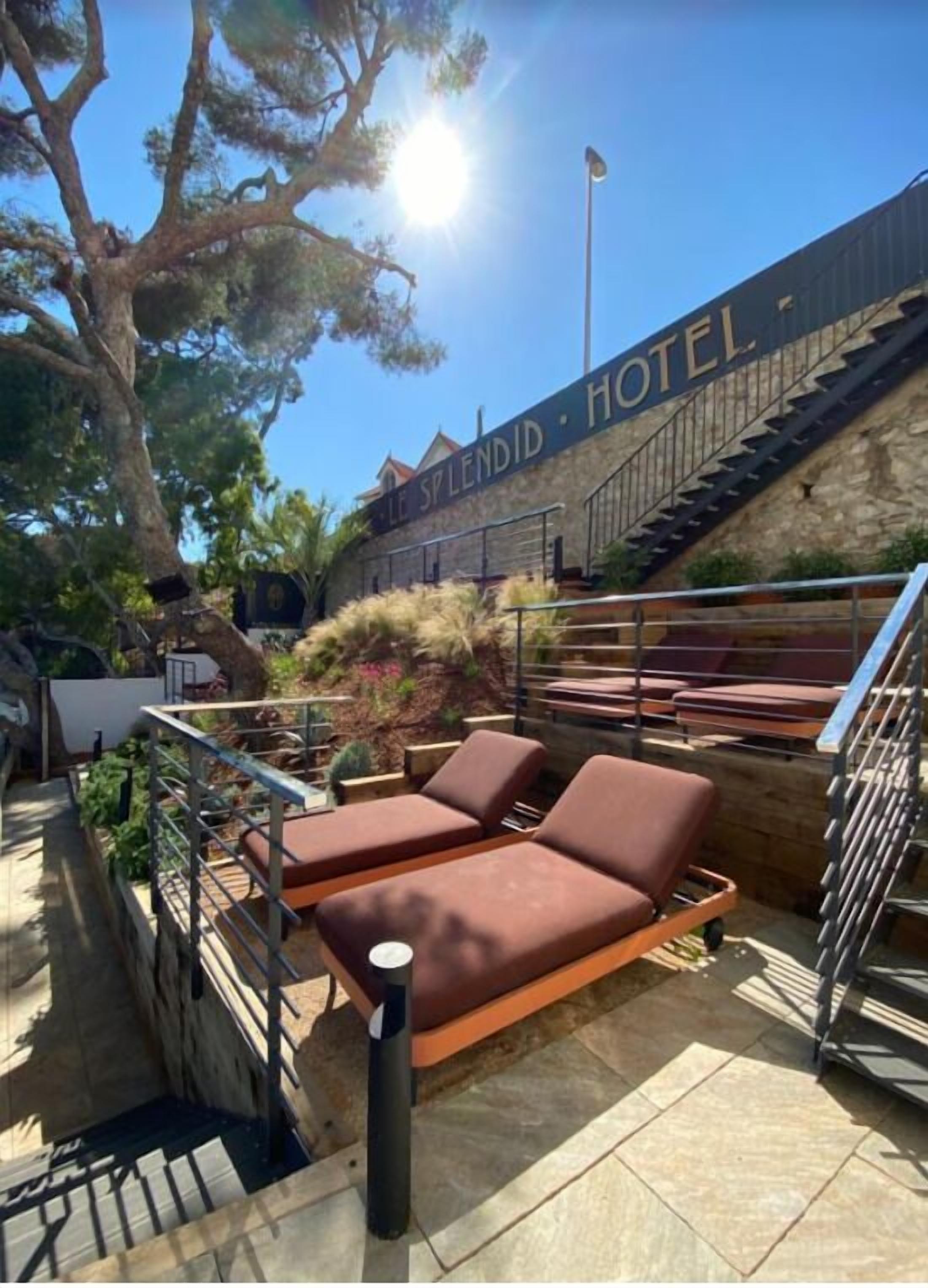 A hotel with a stone facade, outdoor seating area with lounge chairs, and a staircase leading to the entrance.
