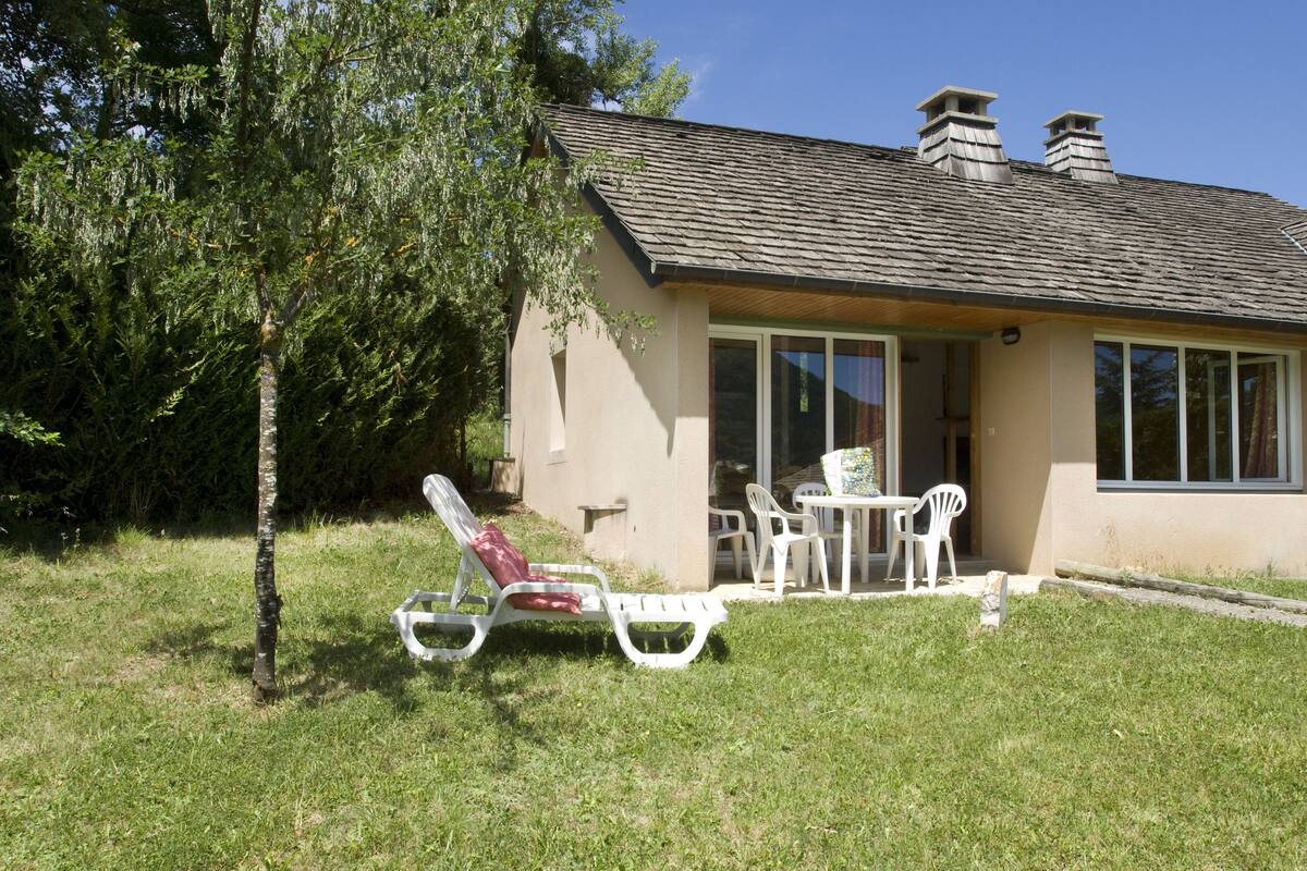 Une maison avec un toit en pente, une véranda avec une table et des chaises, et une pelouse.