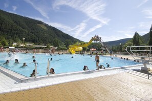 A swimming pool with a water slide, surrounded by a mountainous landscape. - Village de Gites le Colombier (Mende)