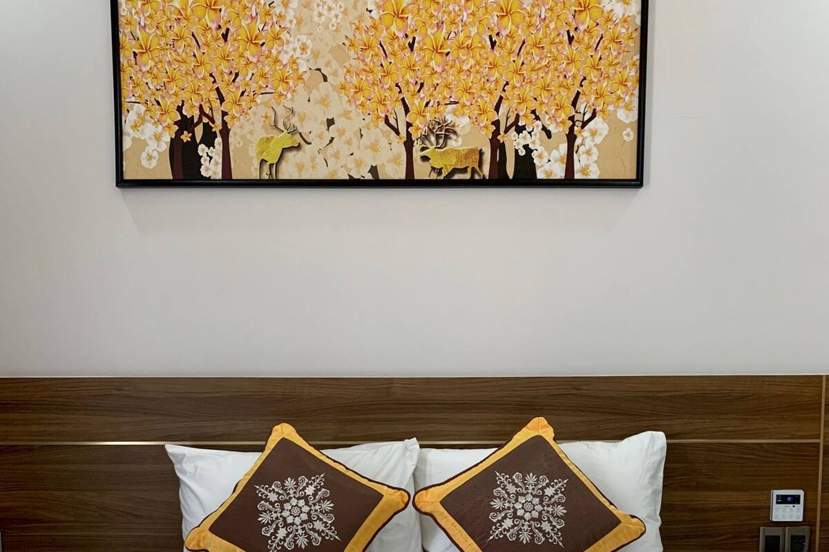 A hotel room with a bed, two decorative pillows, a framed artwork above the bed, and a bedspread with the hotel name.