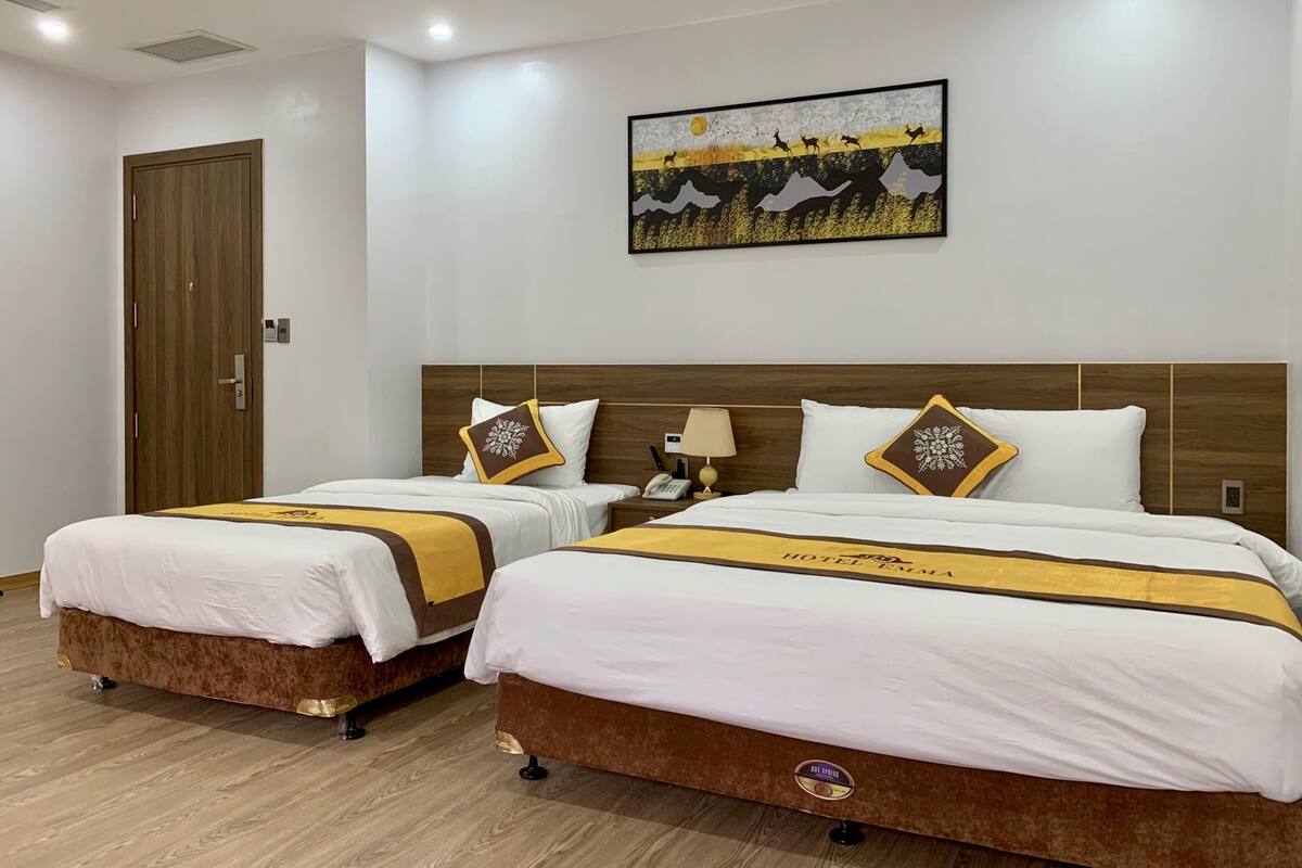 A hotel room with two beds, a wooden door, a nightstand with a lamp, and a painting on the wall.