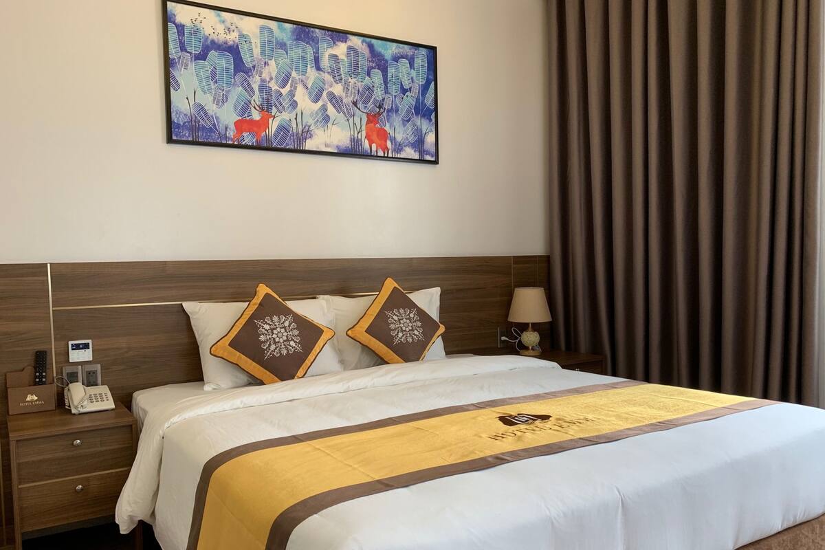 A hotel room with a large bed, two pillows with snowflake designs, a bedside table with a lamp, a phone, and a painting of deer on the wall.