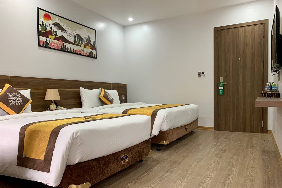 A hotel room with two beds, a wooden headboard, a painting on the wall, and a wooden door.