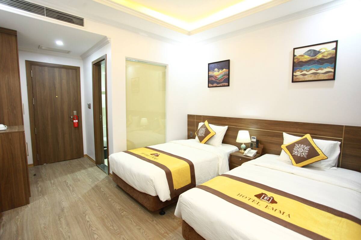 A hotel room with two beds, a wooden wardrobe, a glass door, and artwork on the walls.