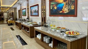 A hotel lobby with marble floors, a buffet counter with various food items, and framed artwork on the walls. - Hotel Emma (Bai Chay)