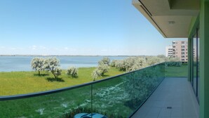 A balcony with a view of a lake, grassy area, and distant buildings. - Apart holiday Athena Mamaia (Constanta)