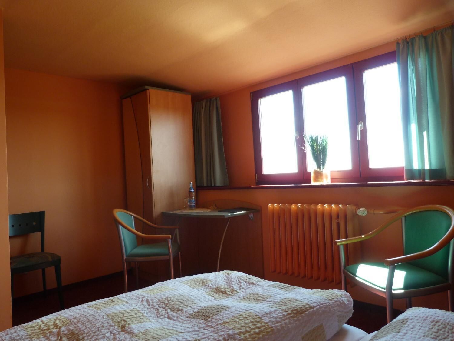 A hotel room with two single beds, a desk with a chair, a radiator, and a window with curtains.