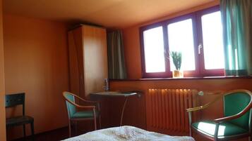 A hotel room with two single beds, a desk with a chair, a radiator, and a window with curtains.