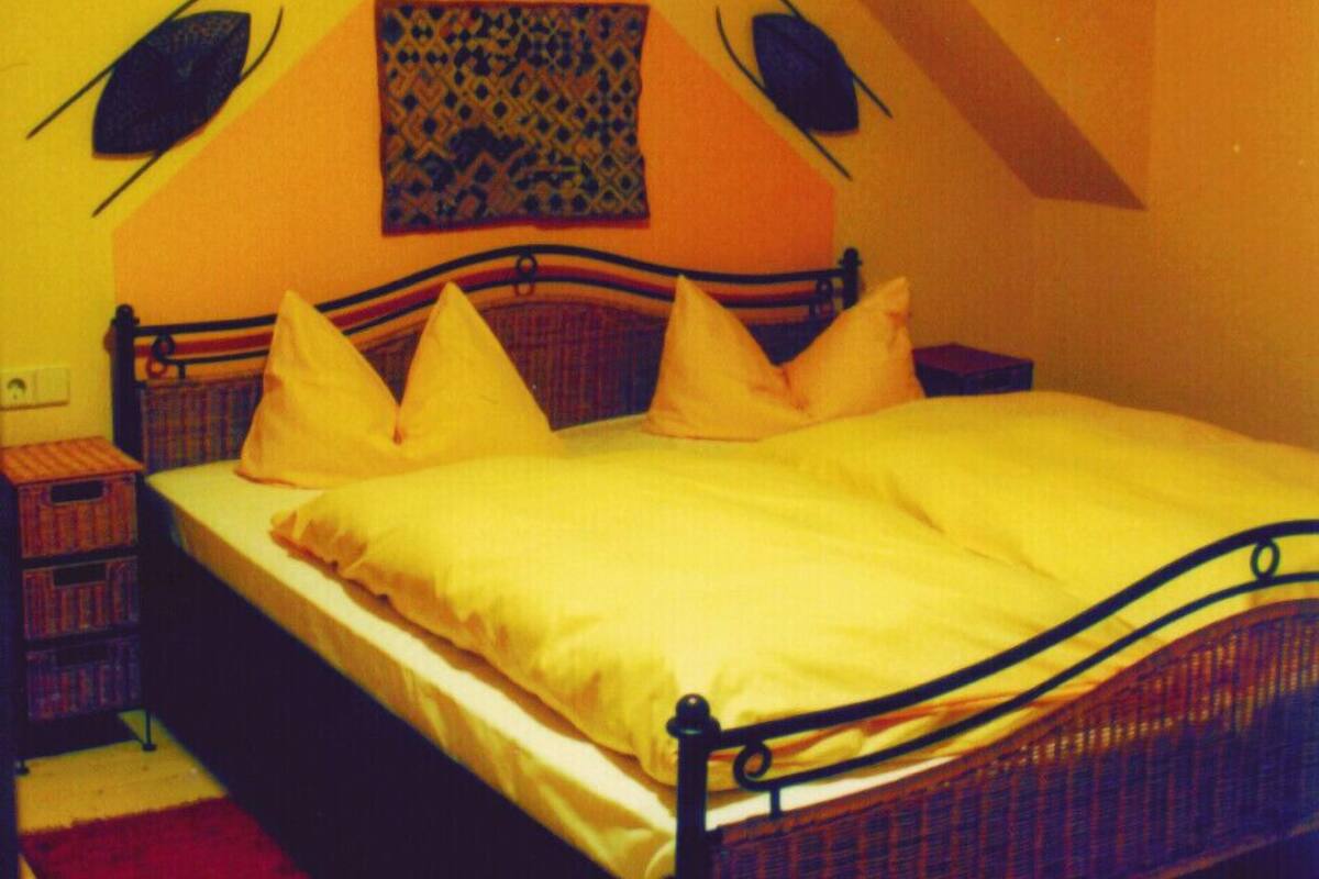 Ein Schlafzimmer mit einem Bett, Kissen, einem Nachttisch, einem roten Teppich und einer Wand mit einem geometrischen Muster.