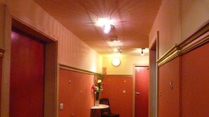 En smal gang med røde vægge og døre, et lille bord med en stol, samt en vase med blomster.